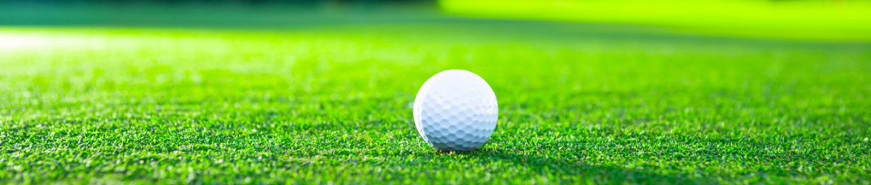 Close up of a white golf ball sitting on green grass at a golf course.